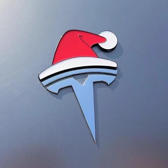 Rød og hvid nissehue monteret på Tesla-emblem på bilens kofanger, tæt på juledekoration