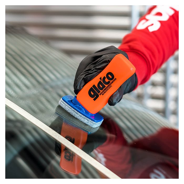 Hånd med Glaco DX glasforsegler på bilrude i nærheden af hvid tape