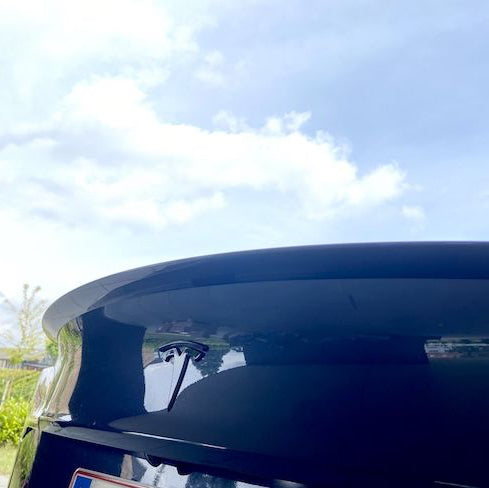 Blank sort ABS-spoiler på bagklappen af en sort Tesla Model Y med blå himmel og skyer spejlet i lakken
