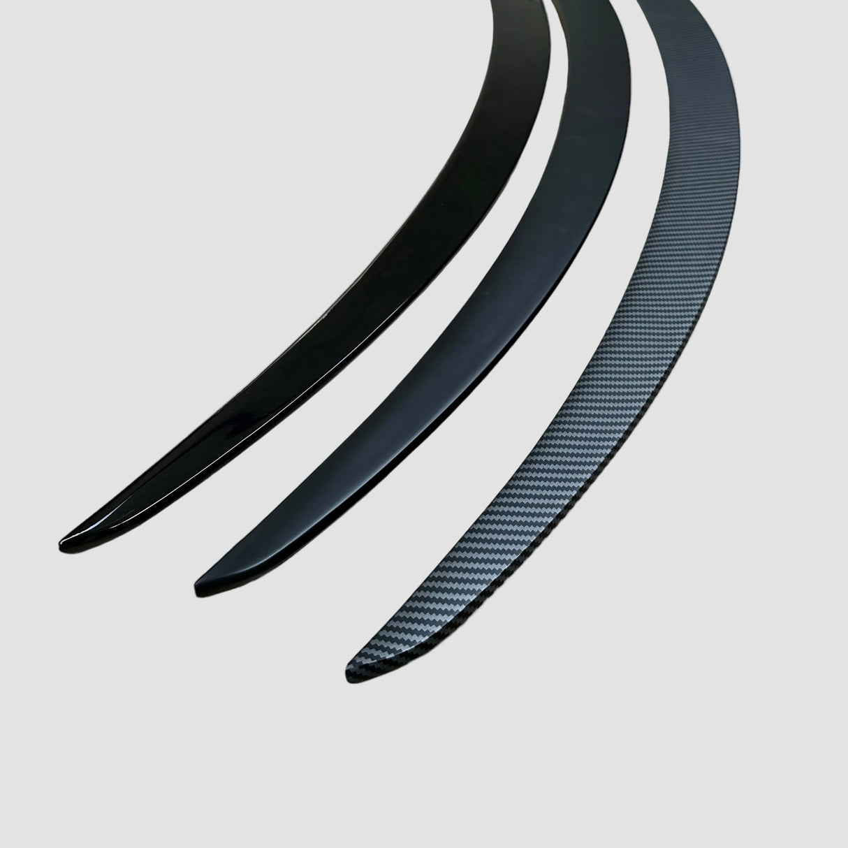 Alle spoiler-varianter til Tesla Model Y i blank sort, mat sort og carbon-look vist ved siden af hinanden på lys baggrund