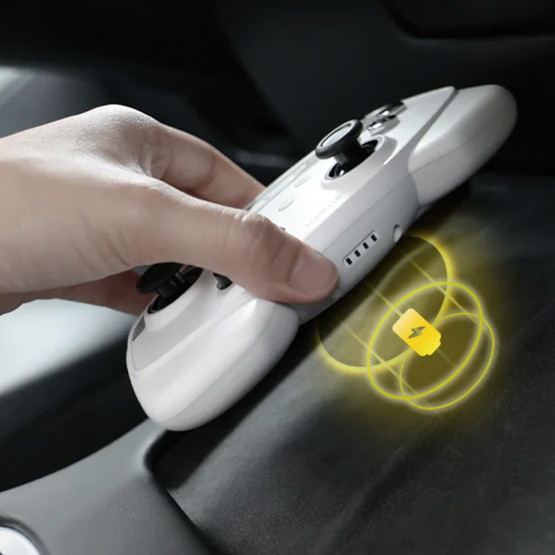 En hånd holder den hvide controller med et lysende gult opladningsikon der illustrerer trådløs opladning