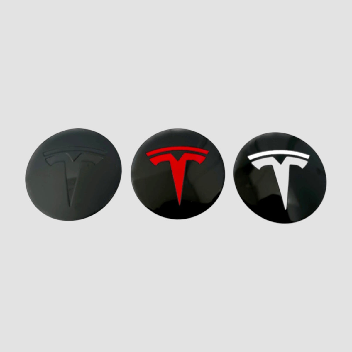 Tre Tesla centerkapsler med T-logo i sort, rødt og hvidt