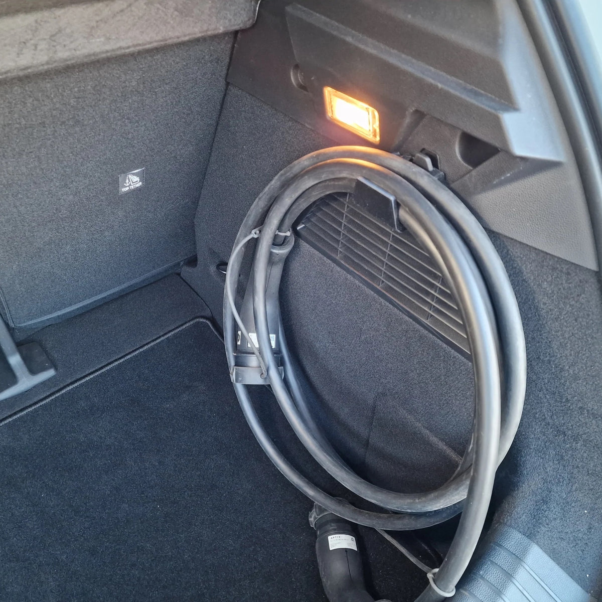 Ladekabel hængt på sort bagagerumskrog i Renault Megane E-tech, nærbillede med orange lys i baggrunden