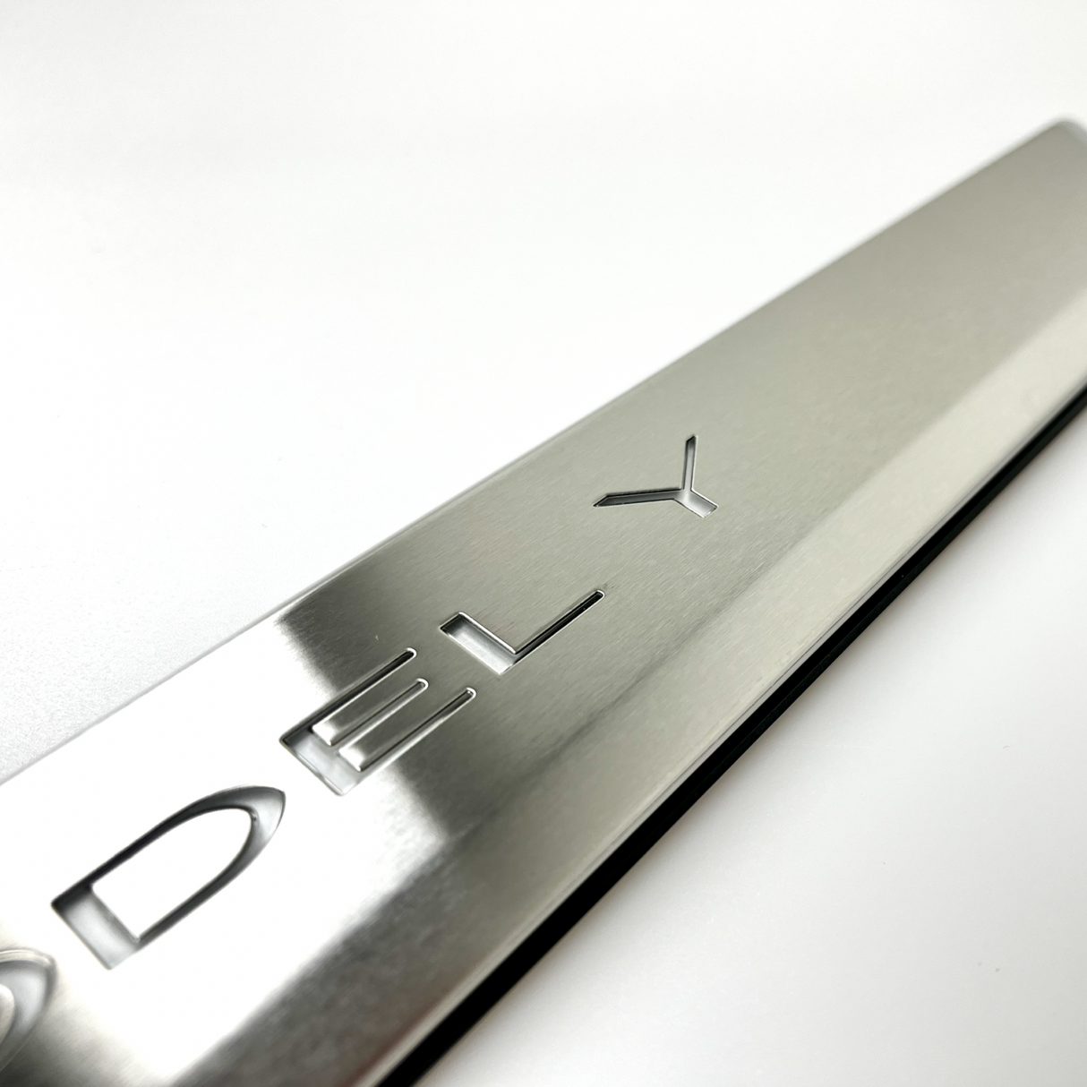 Nærbillede af børstet aluminium-indstigningsliste med 'MODEL Y'-præget tekst, på lys baggrund