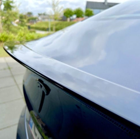 Blank sort ABS-spoiler monteret på bagklappen af en sort Tesla Model Y, set bagfra udendørs