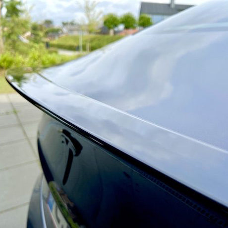 Blank sort ABS-spoiler monteret på bagklappen af en sort Tesla Model Y, set bagfra udendørs