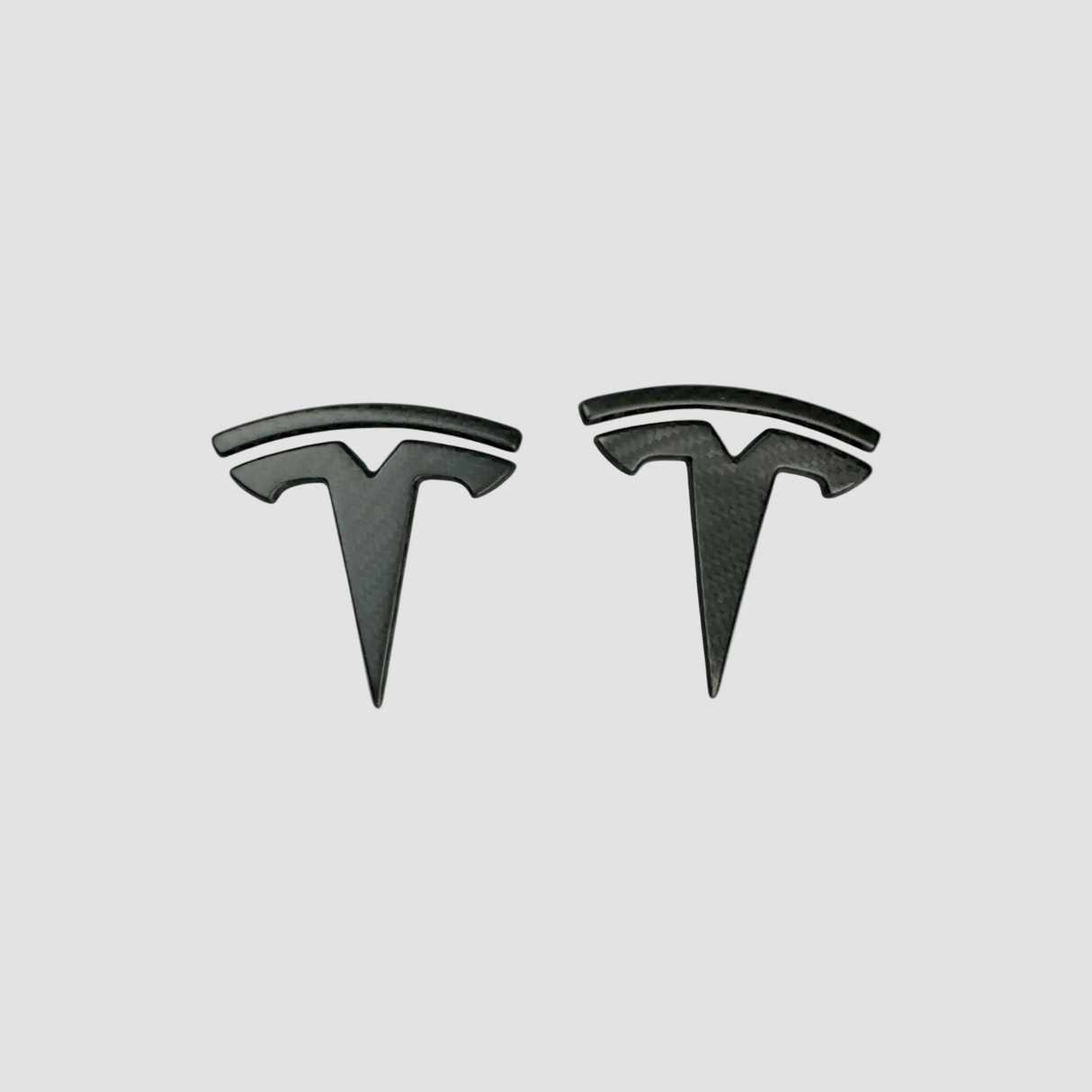 To Tesla-emblemer i ægte mat carbon til Model 3/Y, produktbillede på lys baggrund