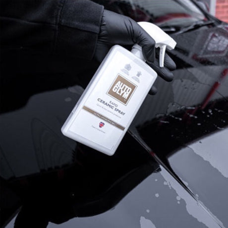 Hånd med handske holder Autoglym Rapid Ceramic Spray, sprøjter på sort billak