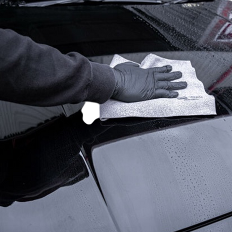 Hånd med handske aftørrer keramisk coating med mikrofiberklud på bilens karrosseri