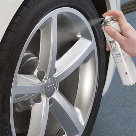 Hånd der sprøjter Autoglym Wheel Protector på bils fælg, viser produktet i brug
