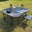 sort campingbord med kaffekrus, børnebøger og en tablet