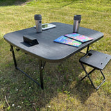sort campingbord med kaffekrus, børnebøger og en tablet