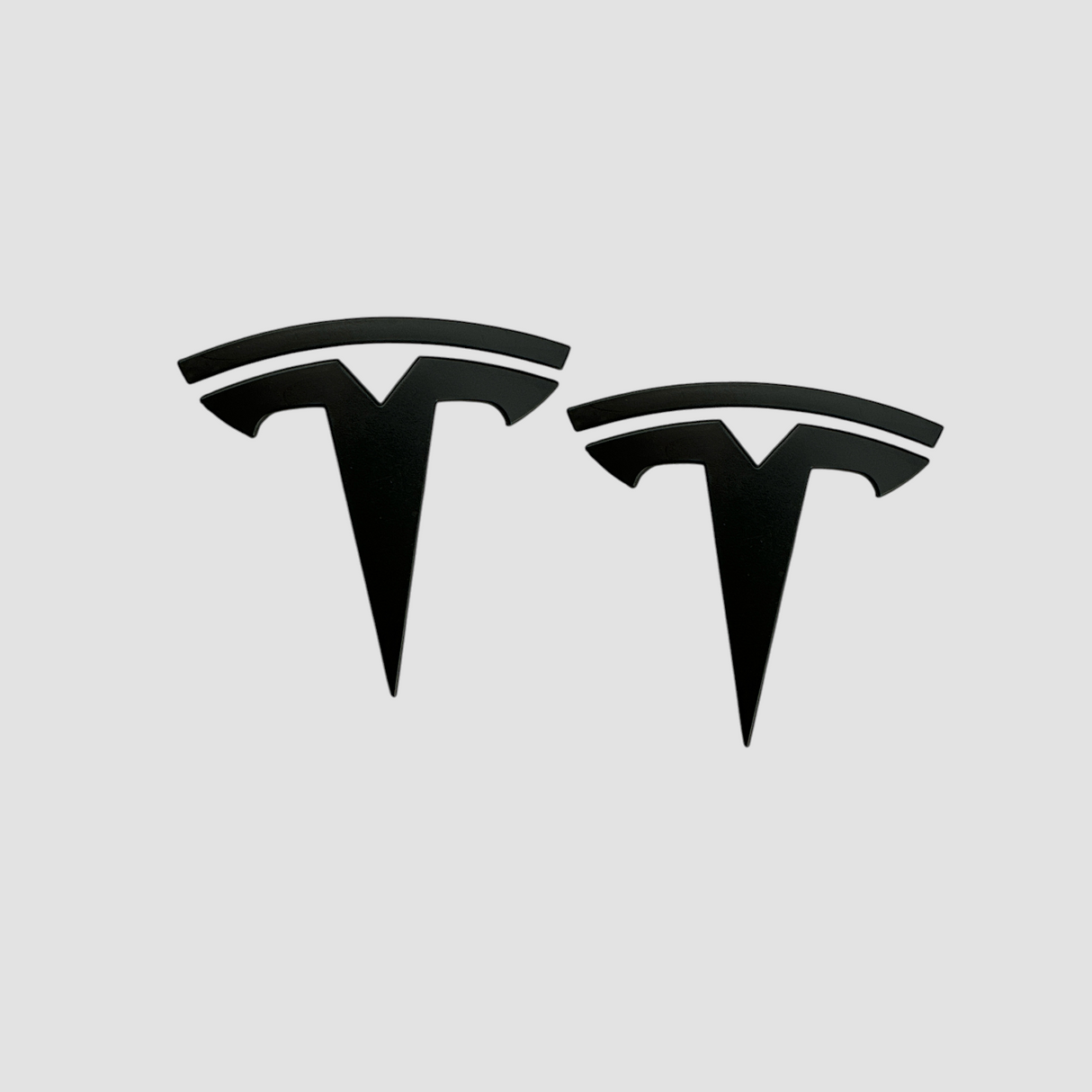 To sorte Tesla T-emblemer i ABS til Model 3/Y, produktbillede på lys baggrund
