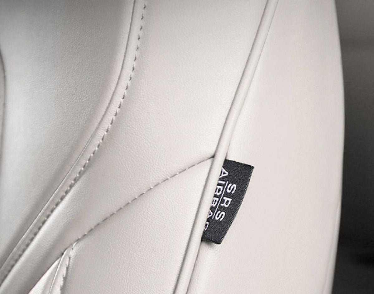 Nærbillede af det hvide læder-sædeovertræks sømme og et SRS Airbag-mærke i siden
