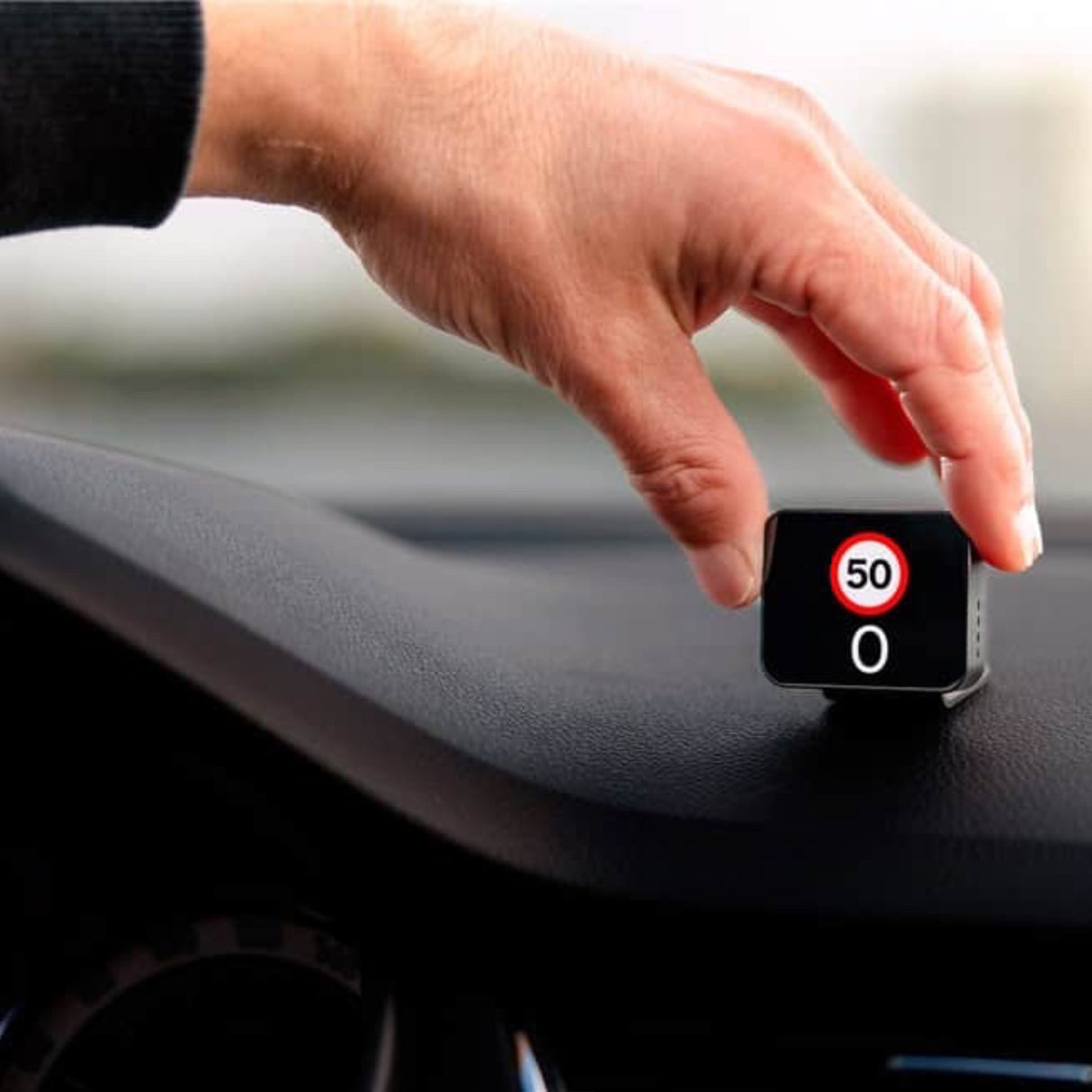 Hånd placerer Saphe T trafikalarm på instrumentbrættet, viser hastighedsgrænse 50