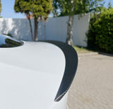 Spoiler i carbon-look monteret på bagklappen af en hvid Tesla Model Y, udendørs