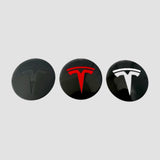 Tre Tesla centerkapsler med T-logo i sort, rødt og hvidt