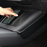 En hånd lægger en telefon på det sorte cover til den trådløse oplader i en Tesla Model 3 Highland