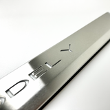 Nærbillede af børstet aluminium-indstigningsliste med 'MODEL Y'-præget tekst, på lys baggrund