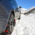 Snekæder monteret på et gråt bildæk i sneklædte bjerge