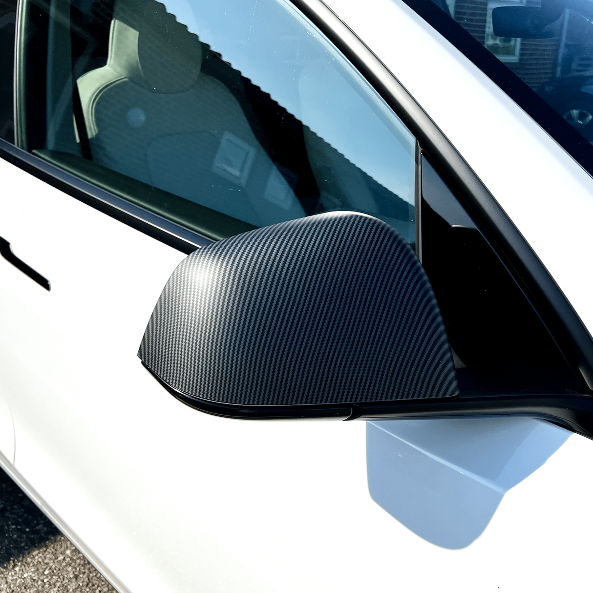 Cover i carbon-look monteret på sidespejlet på en hvid Tesla Model Y